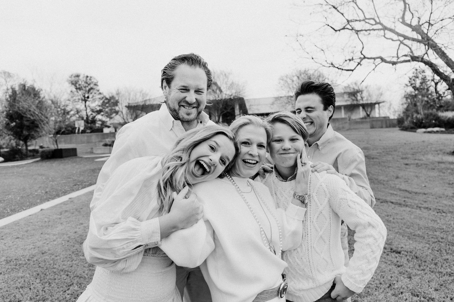 Black and white photo of a joyful family of five hugging outdoors.