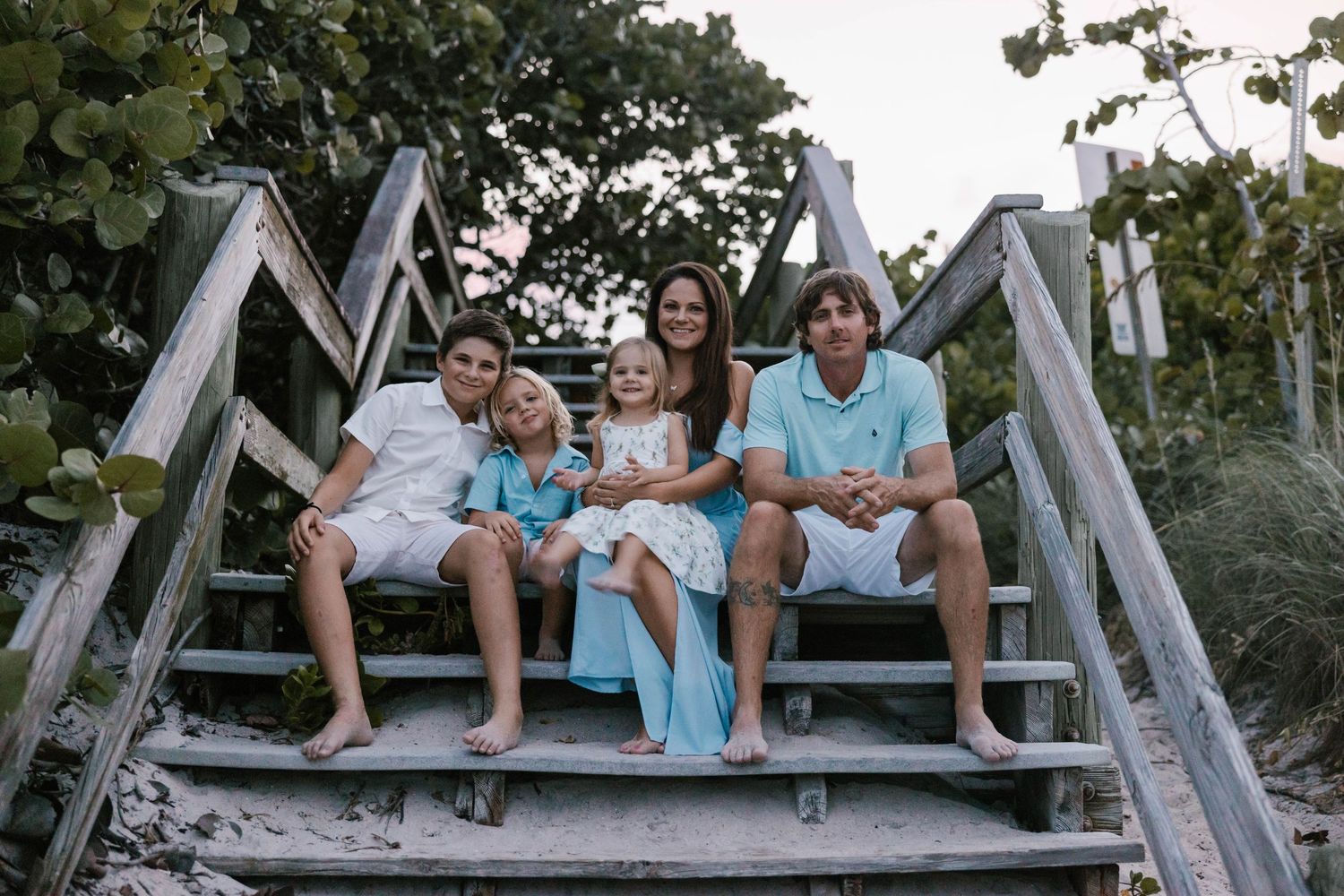 A happy family of five sitting together on wooden beach stairs at sunset.