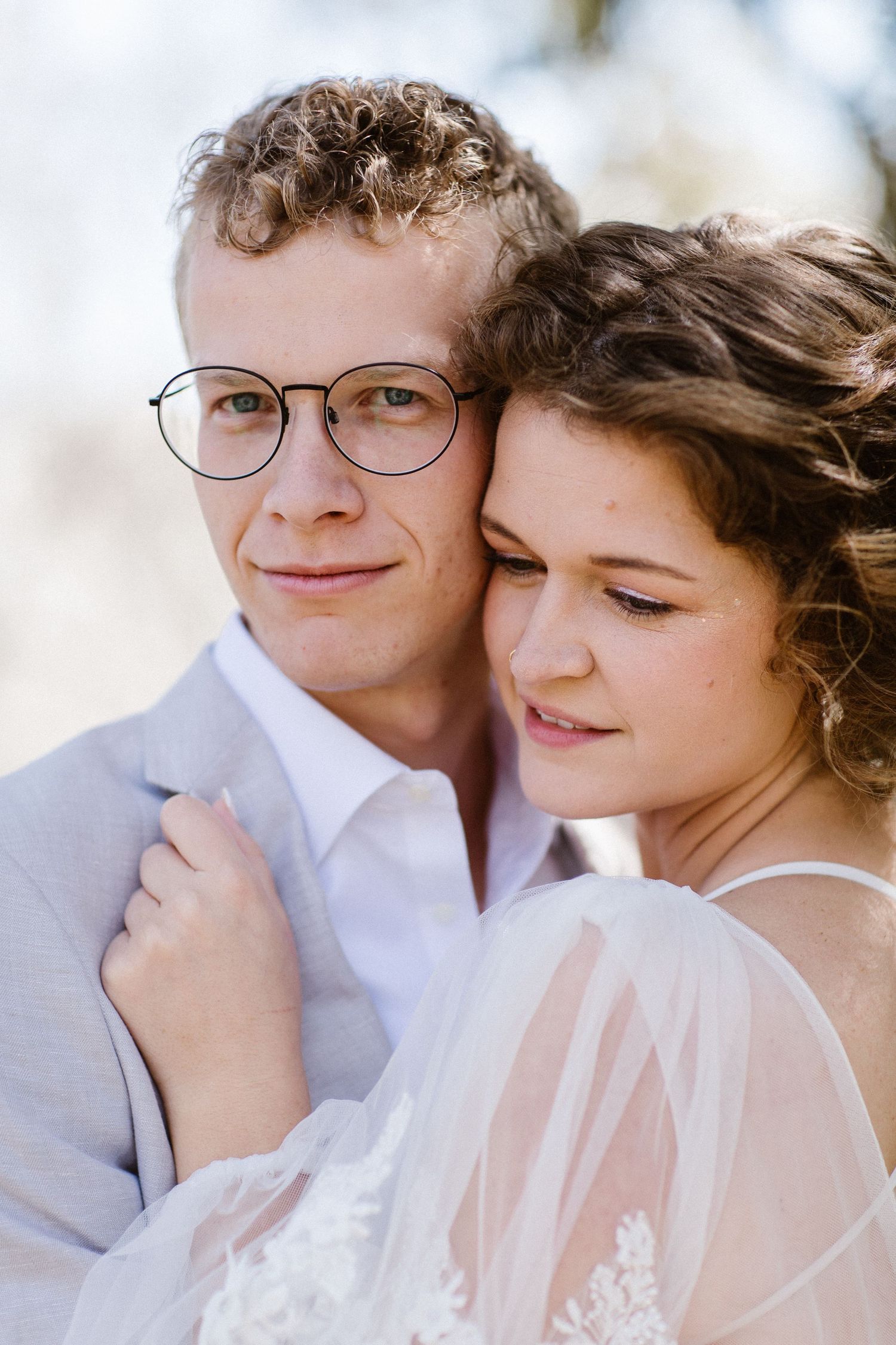 Close-up portrait of groom in glasses and bride leaning together tenderly in natural light.