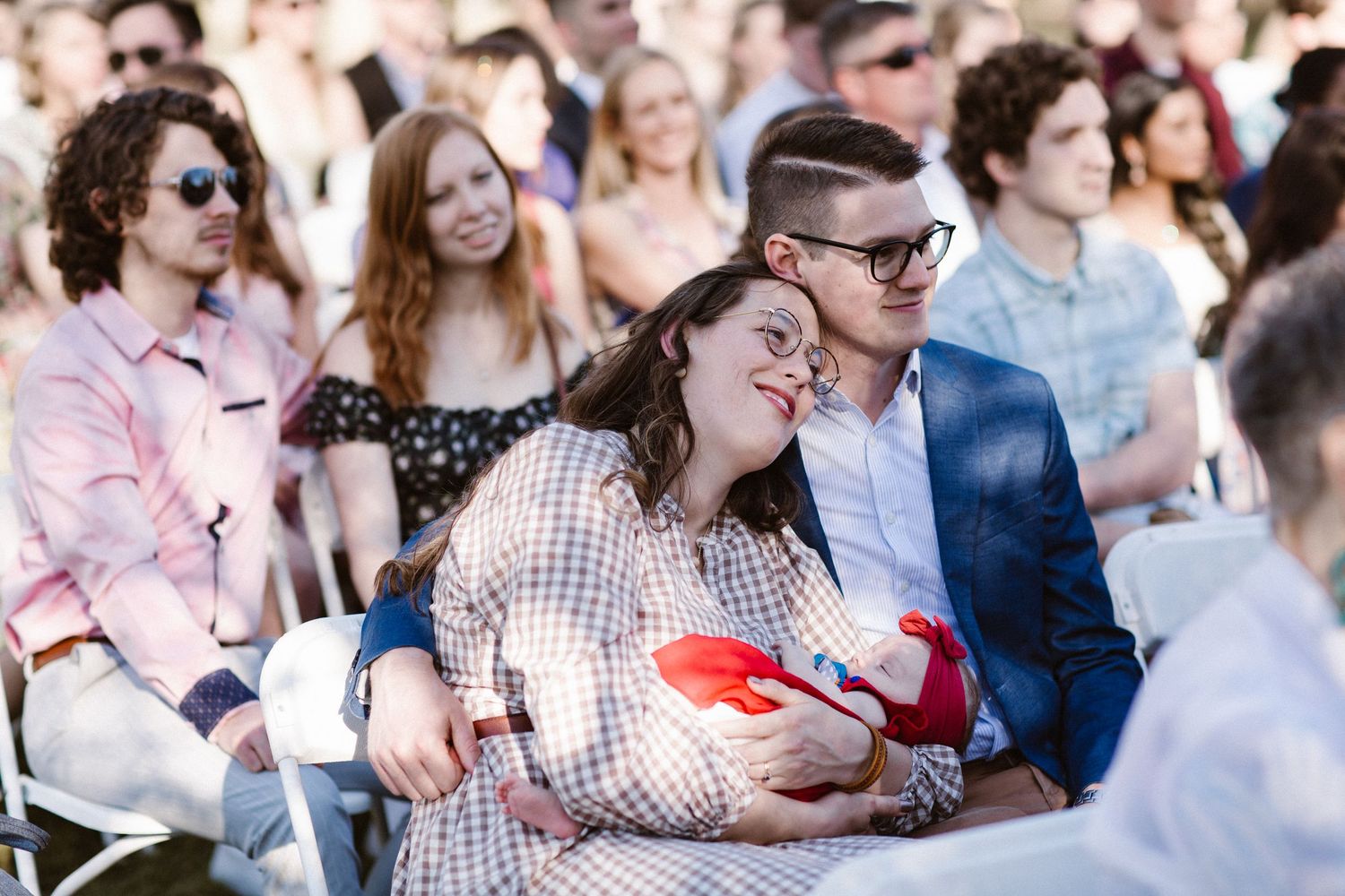 A smiling couple sits together at an outdoor wedding ceremony, woman holding a toy lobster.
