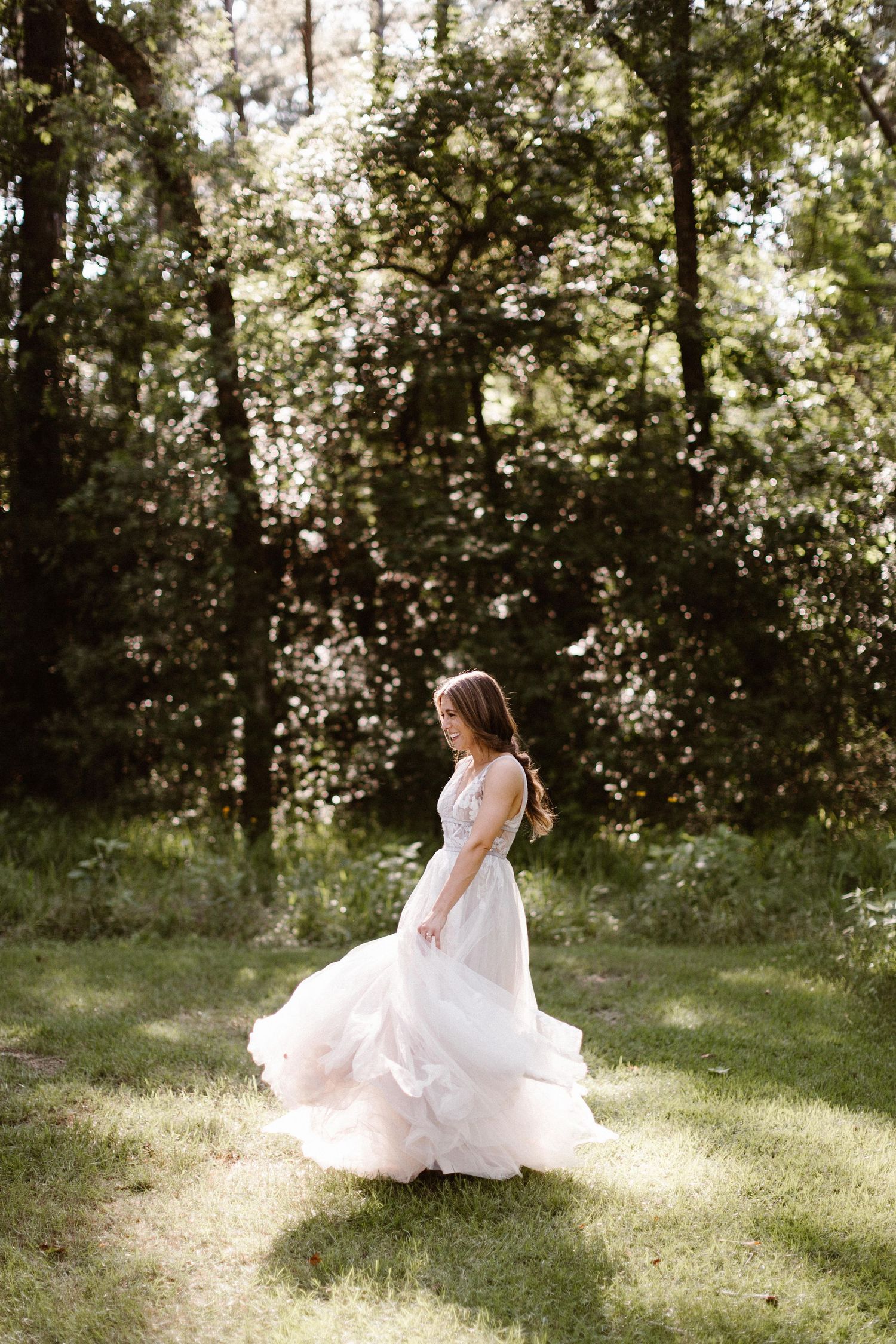 Bride twirling in a flowing blush tulle wedding gown in a sunlit forest clearing.