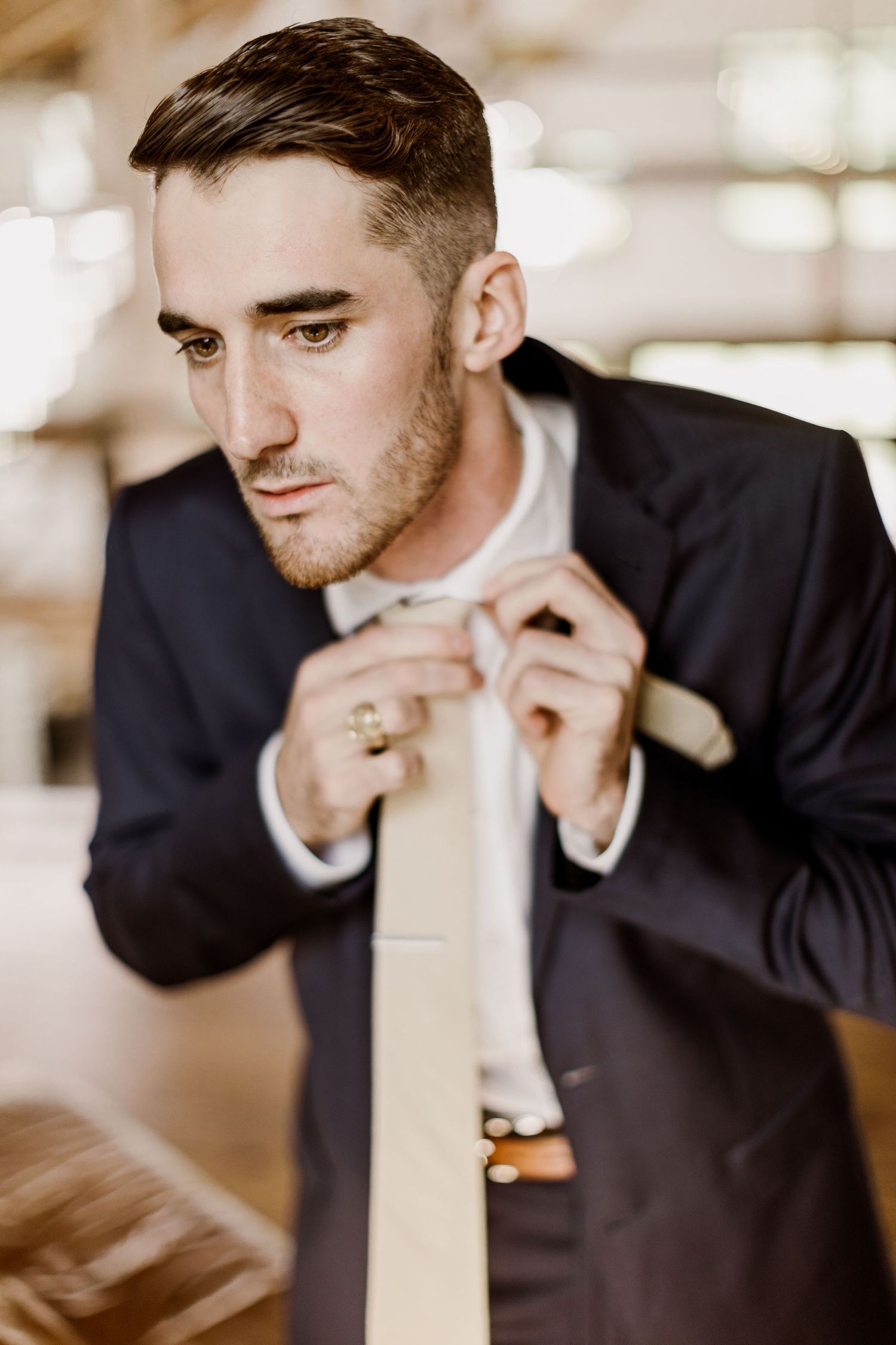 Dapper groom in navy suit adjusts his beige tie while getting ready for his wedding day.
