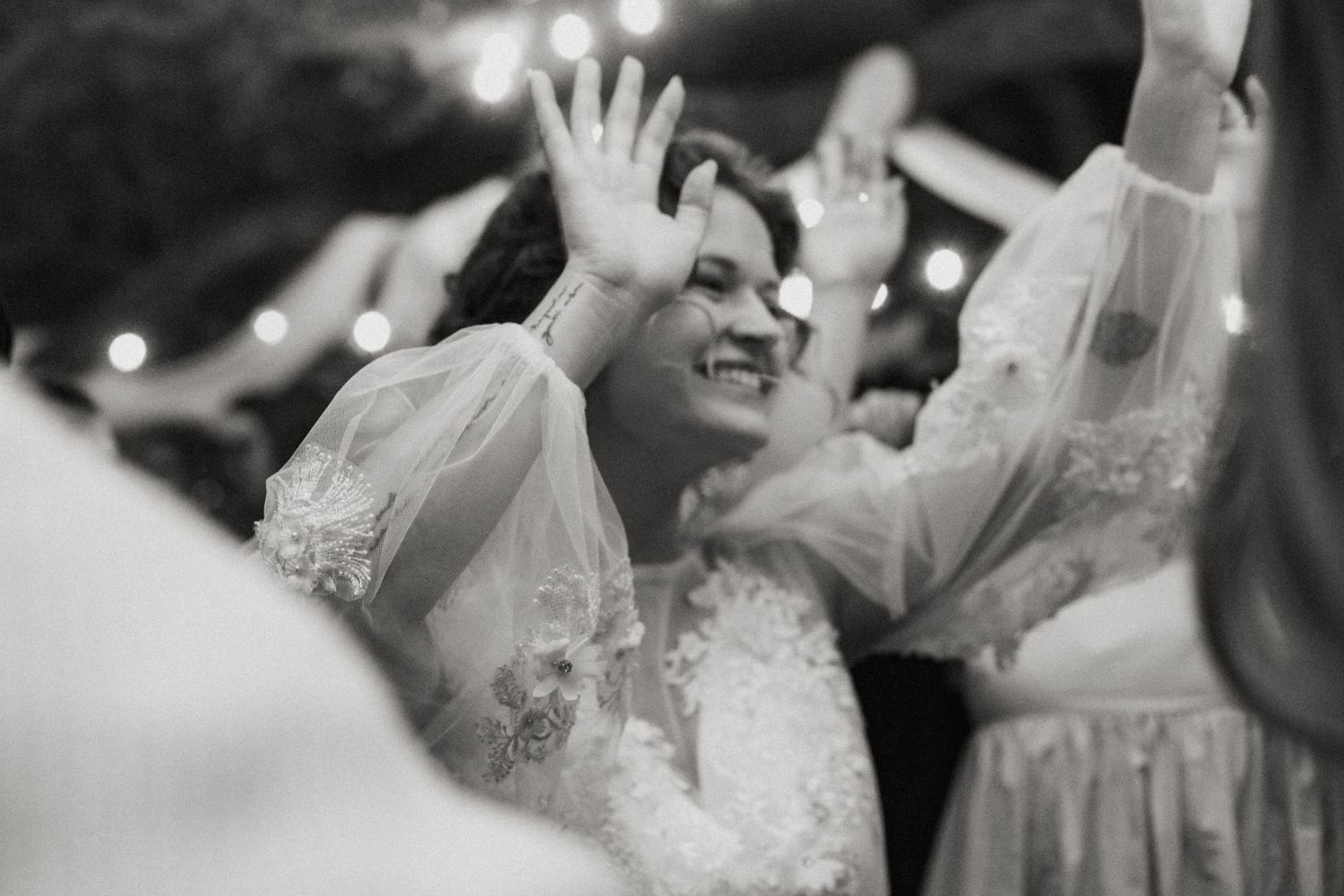 Black and white photo of a bride smiling and dancing with hands raised at reception.
