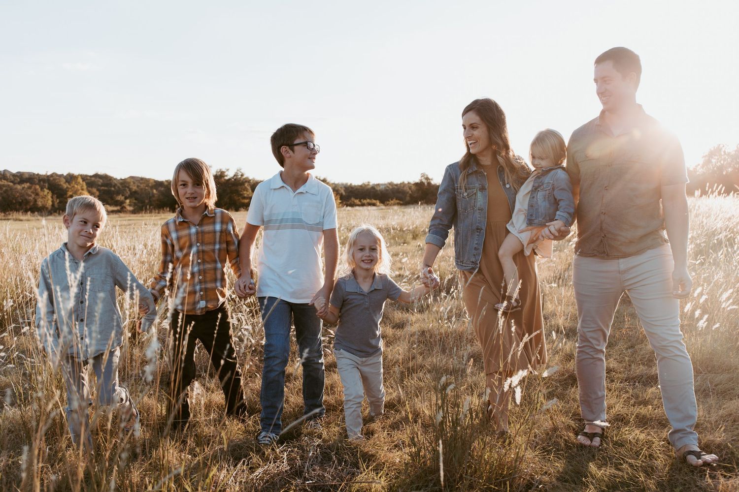 Large family with six children walking together through a sunny golden field at sunset.