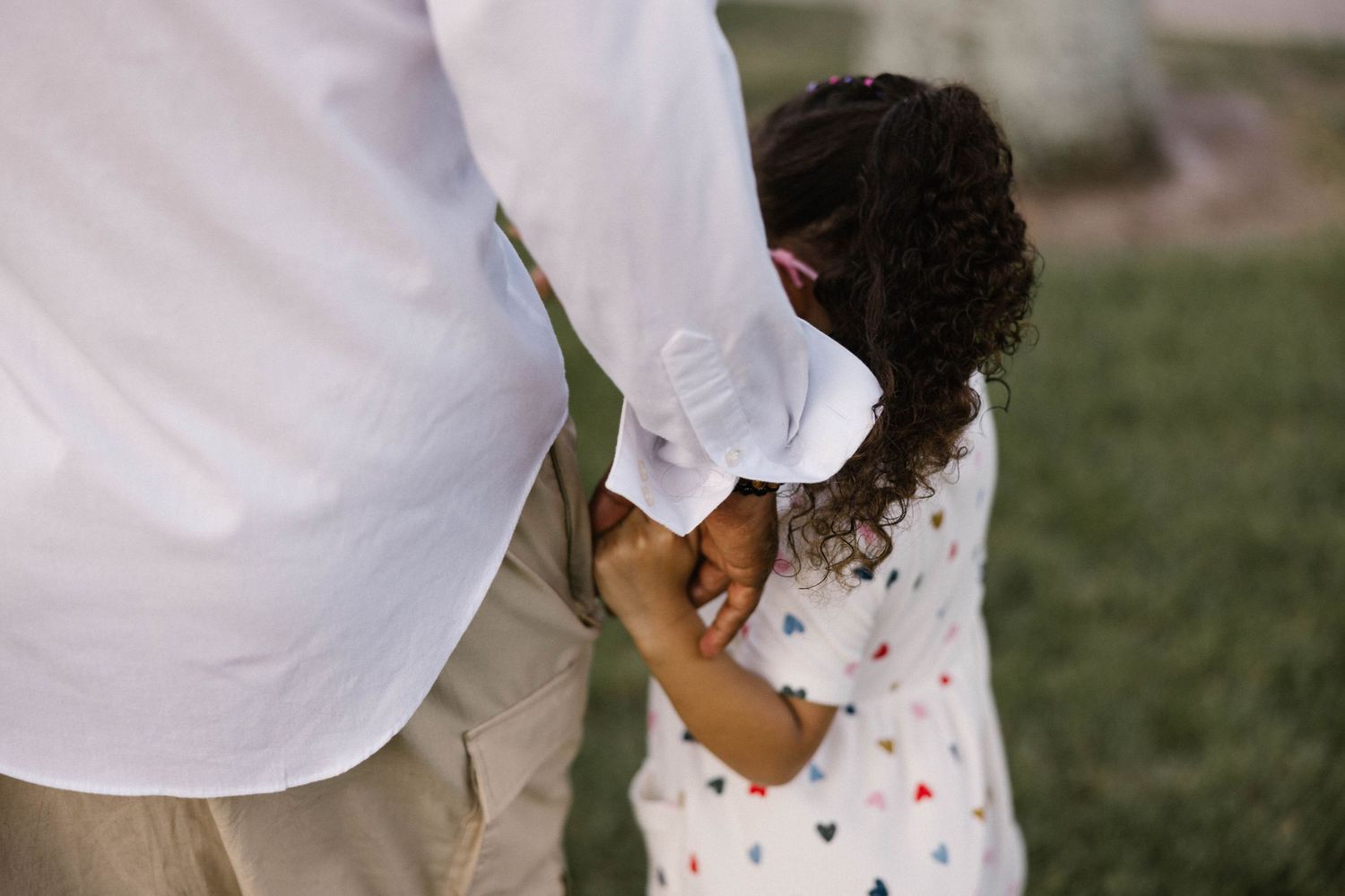 A child in a heart-print shirt holds an adult's hand while standing on green grass.
