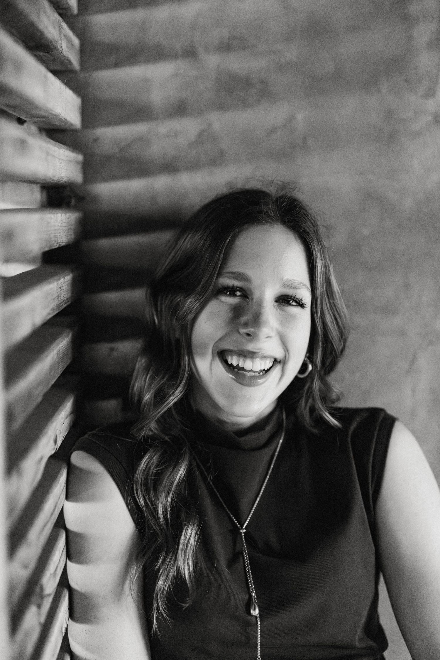 Black and white portrait of smiling brunette woman leaning against wooden slats.