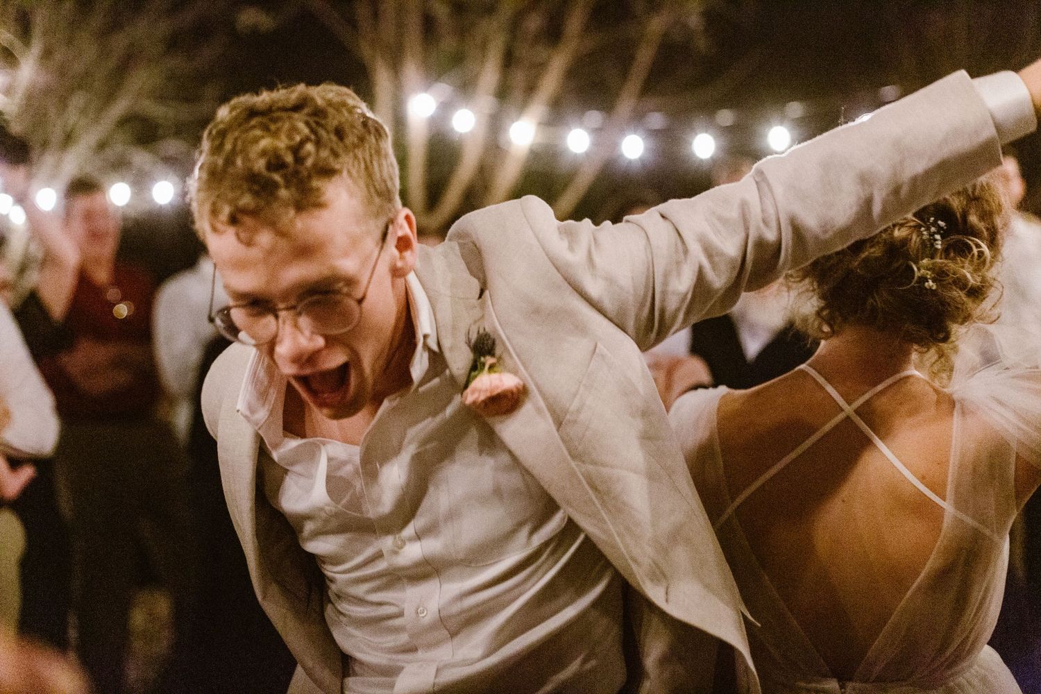 Groom dancing energetically with bride at lively outdoor evening wedding reception.