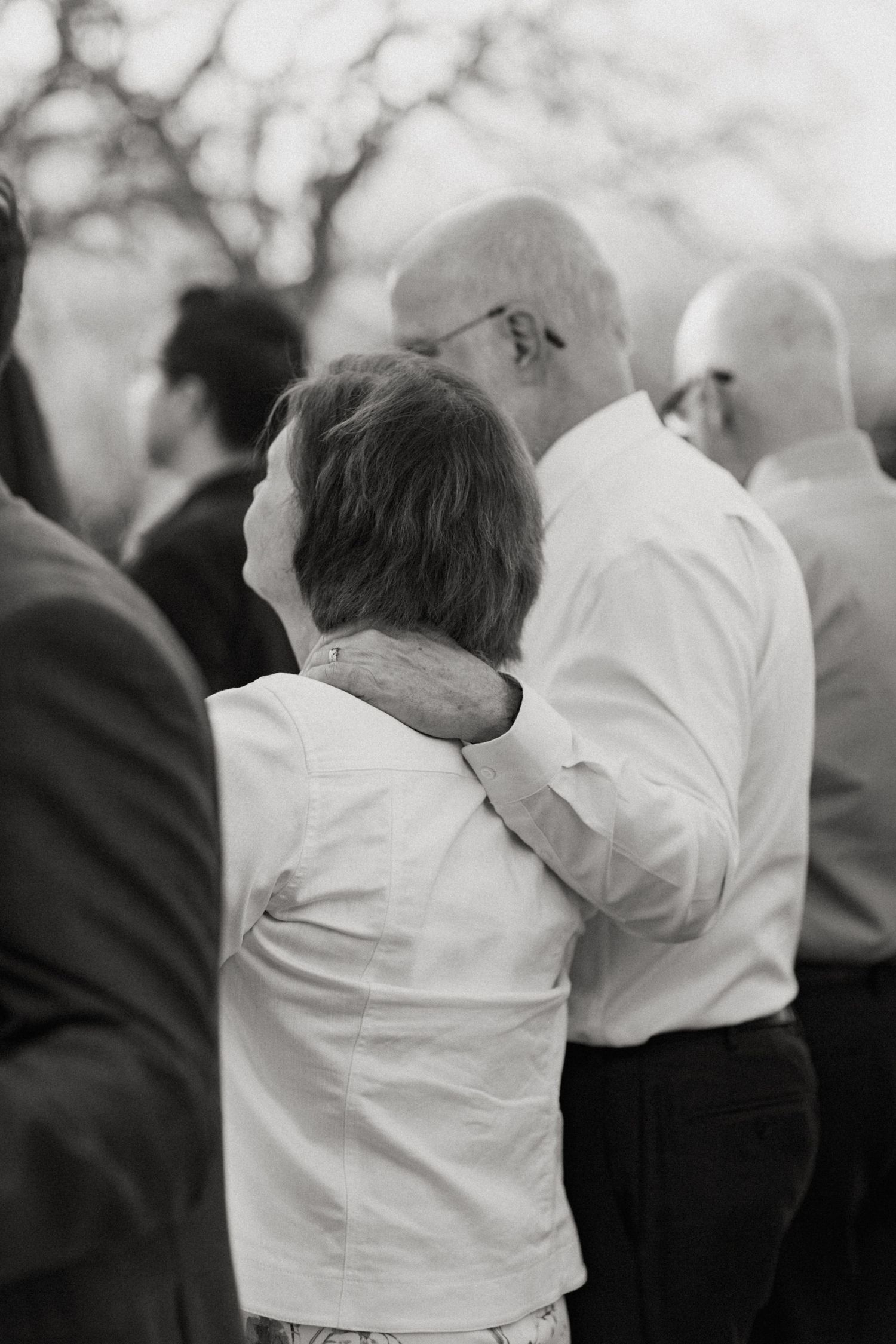 Black and white photo of elderly couple sharing tender moment with mans arm around womans shoulder.