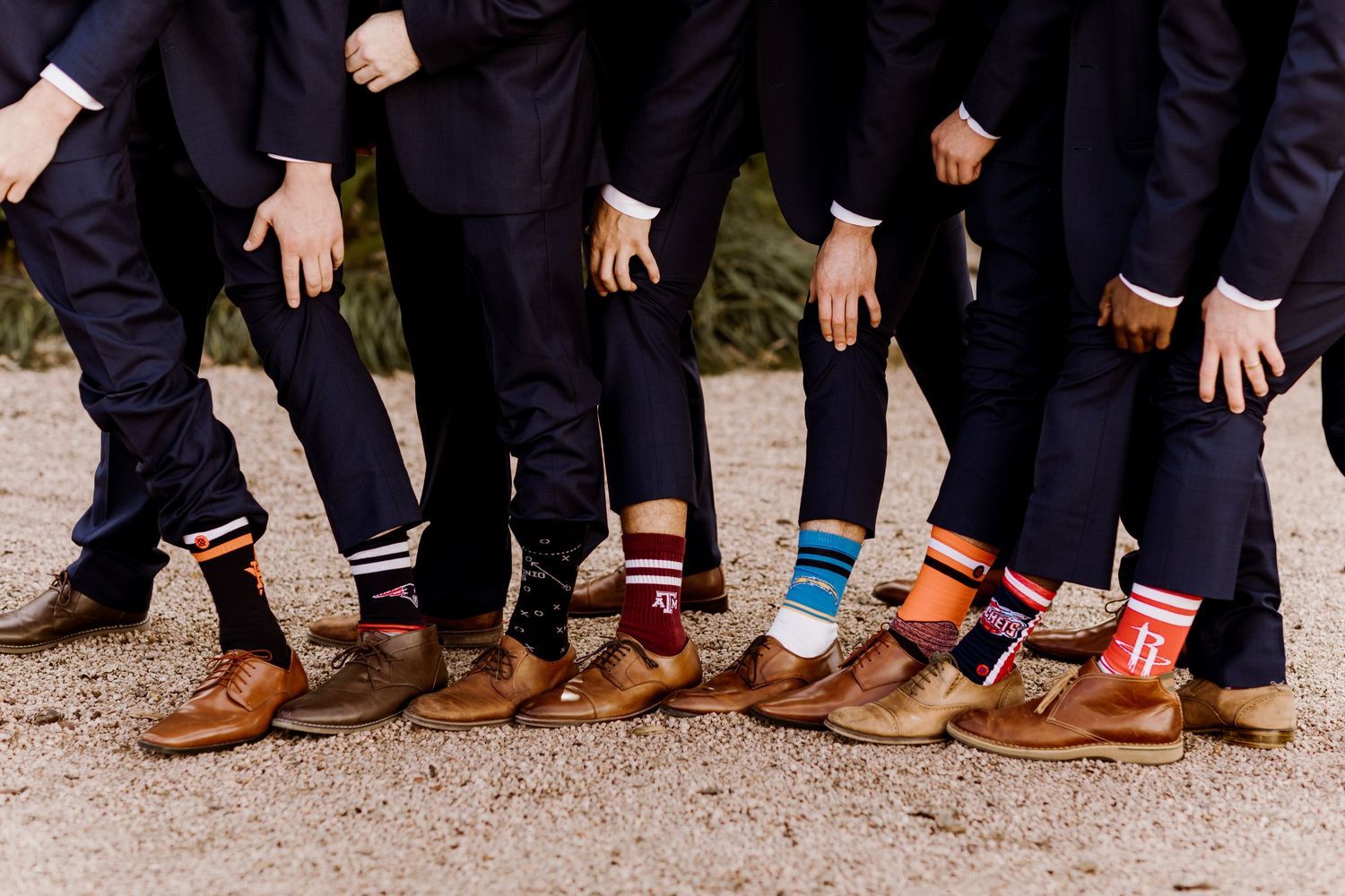 Groomsmen showing off colorful mismatched fun wedding socks with brown leather shoes at outdoor ceremony.