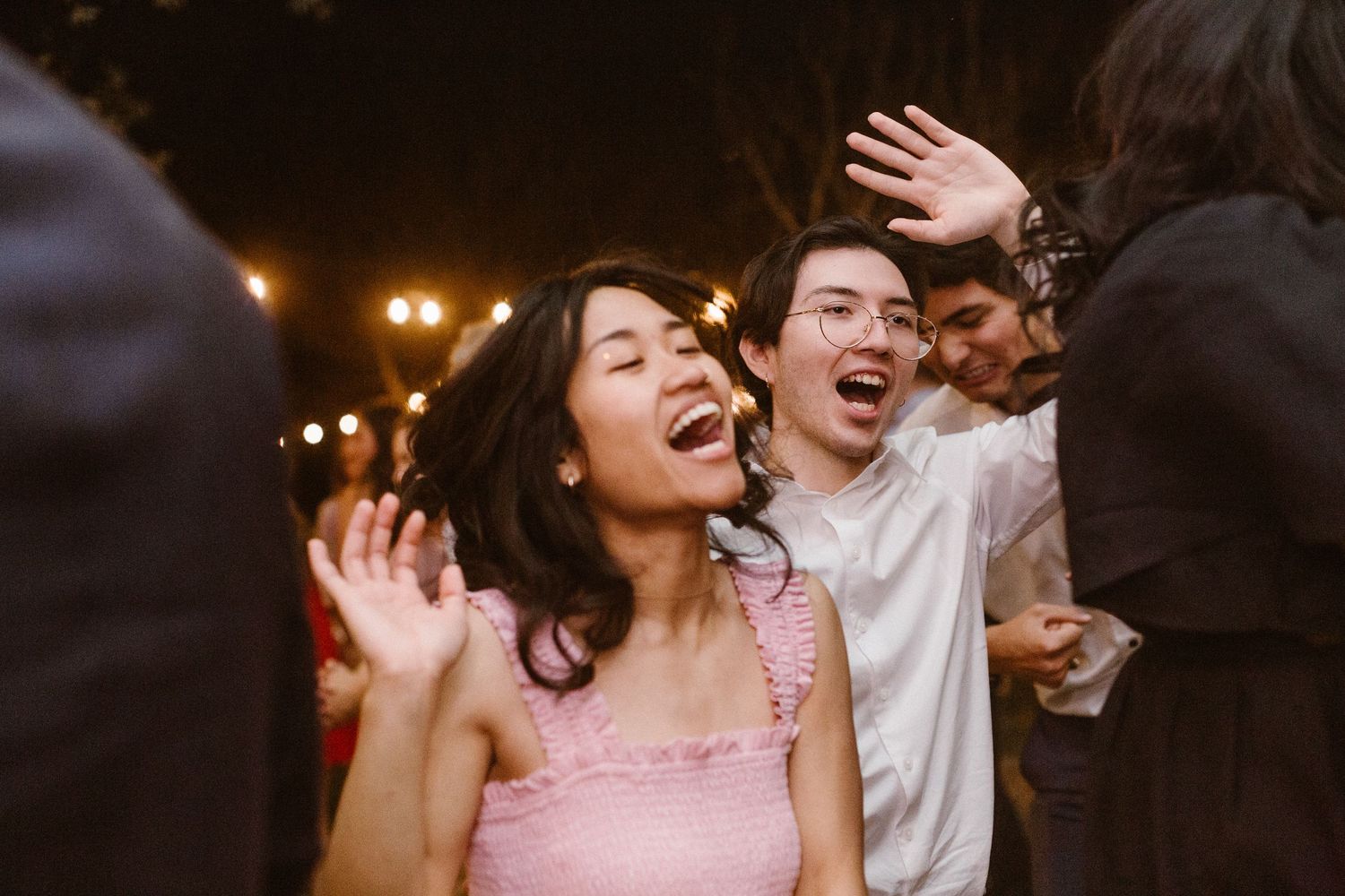 Woman in pink dress laughing joyfully while dancing at an outdoor evening reception.