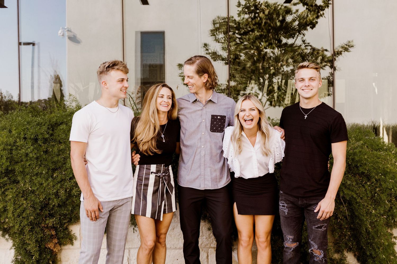 Five young adults smiling and laughing together outdoors in a group photo.