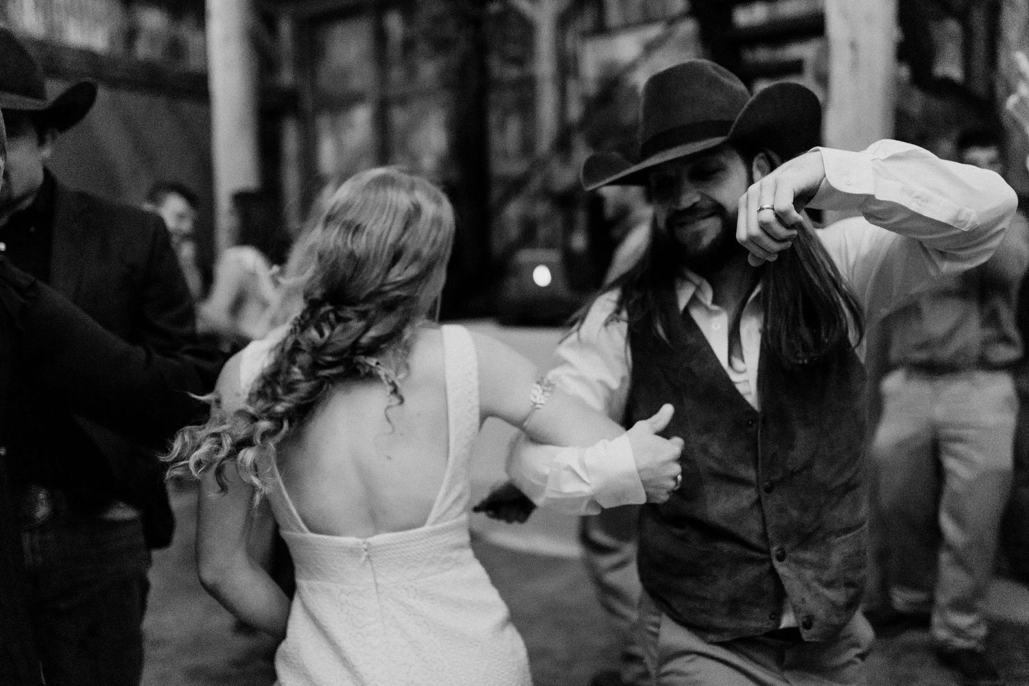 Black and white photo of bride and groom dancing at wedding reception, groom wearing cowboy hat.