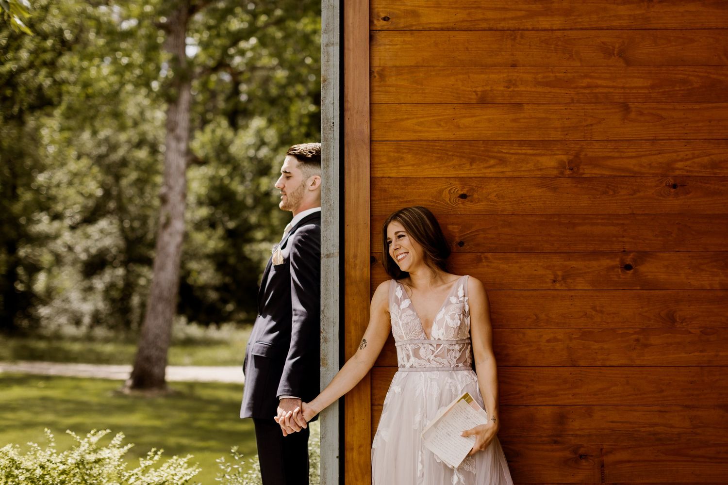 Bride and groom holding hands beside a wooden wall in a garden setting.