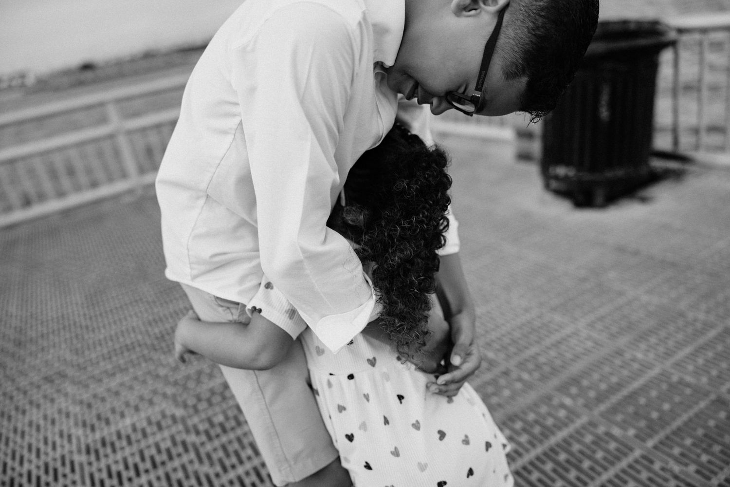 Black and white photo of father tenderly embracing his young daughter on an outdoor pier.