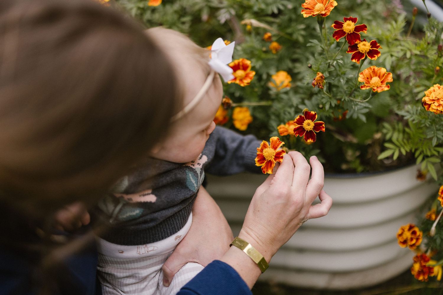 Mother holding child while pointing at vibrant orange and yellow marigolds in garden planter.