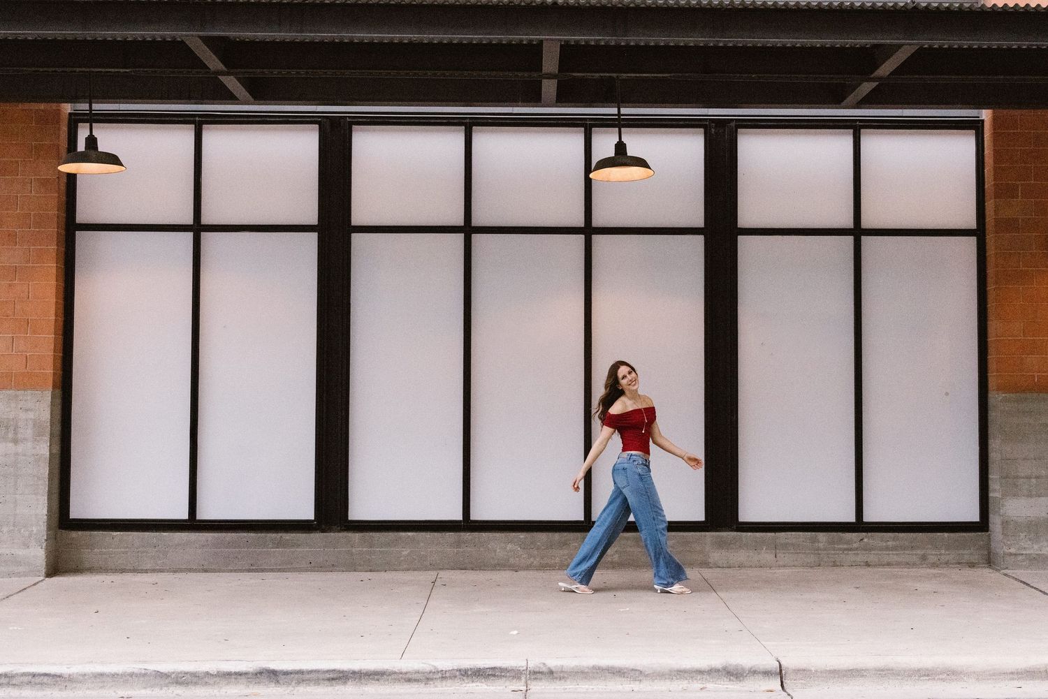 Young woman in red crop top and wide-leg jeans walking past large storefront windows.