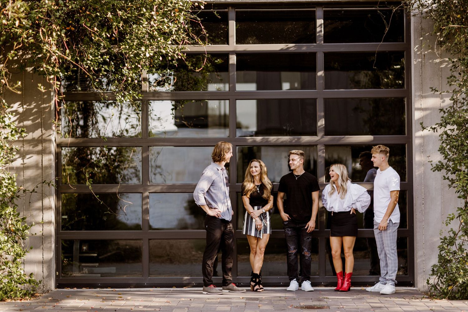Five young adults in trendy outfits chatting outside near a glass garage door.