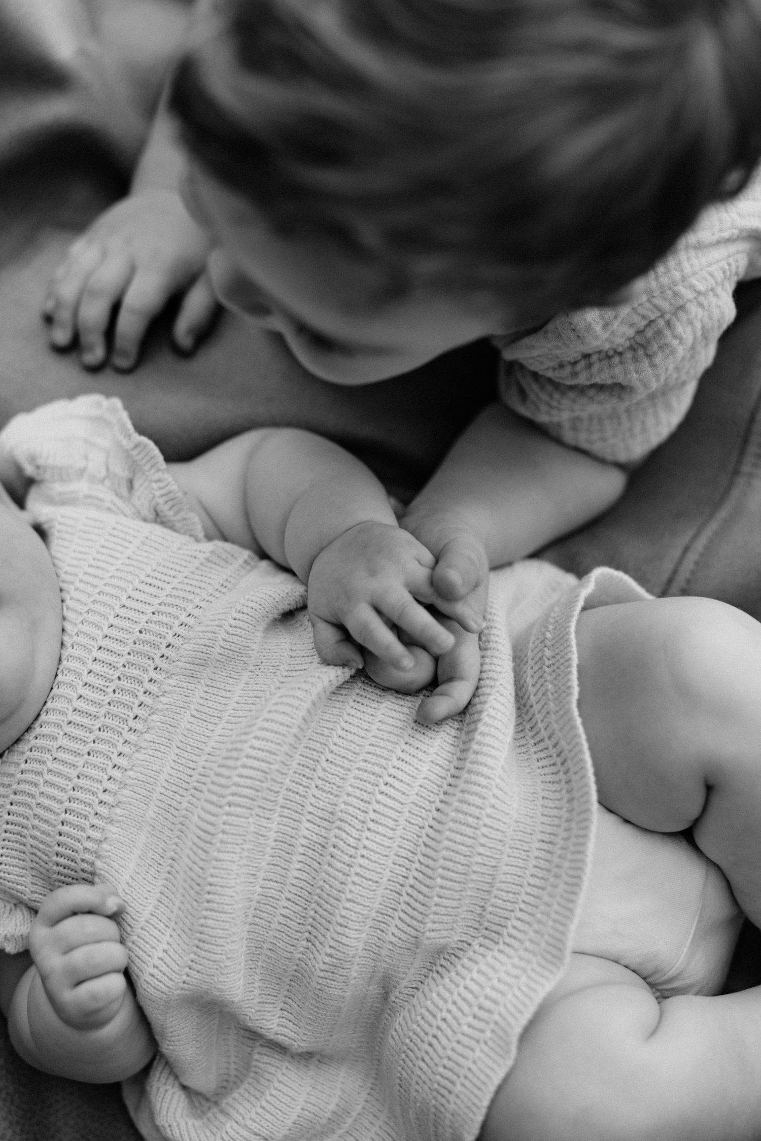 Sweet black and white photo of a toddler gently holding hands with a newborn baby sibling.