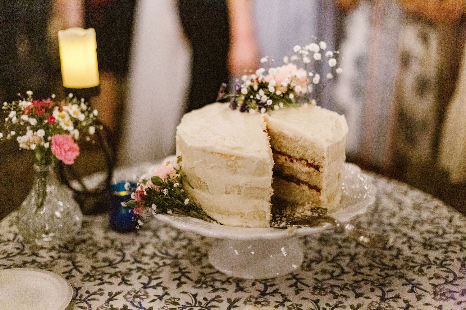 Elegant single-tier white naked wedding cake with baby's breath flowers on decorative stand.