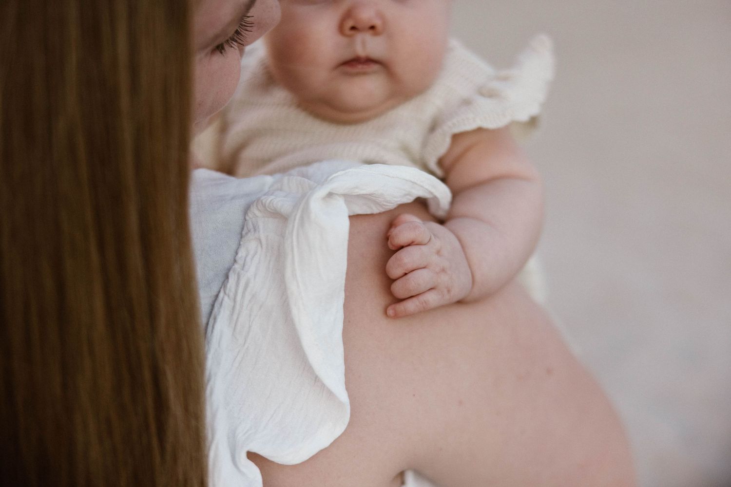 Close-up of a newborn baby in white muslin cloth being held over mothers shoulder.