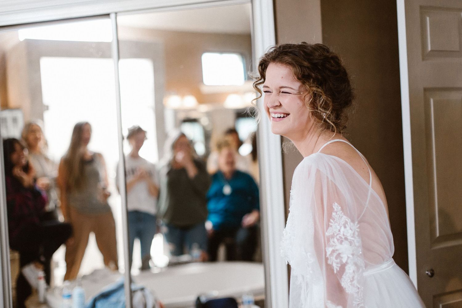 Radiant bride smiling in her wedding dress while bridesmaids admire her in the background.