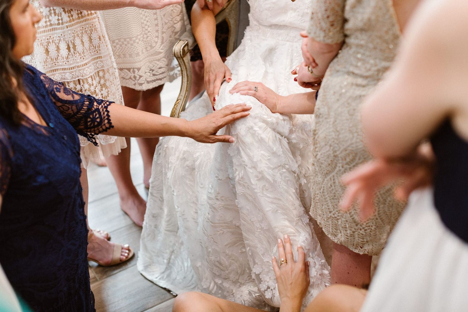 Bridesmaids helping bride into lace wedding gown during wedding day preparations.
