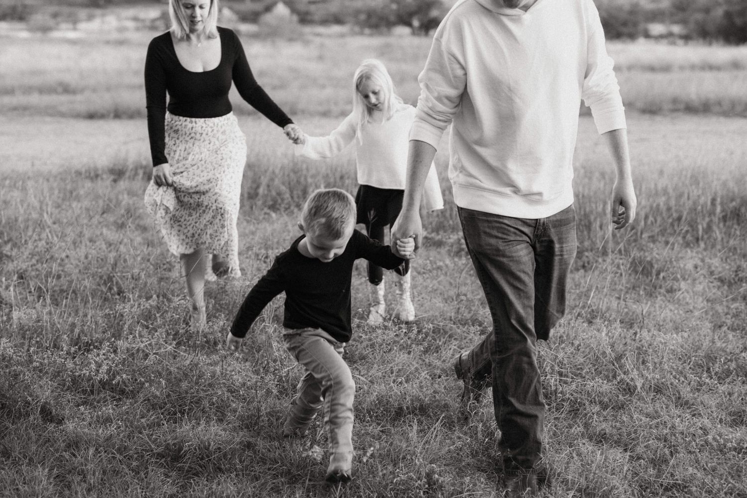 Black and white candid photo of a family walking together through a grassy field.