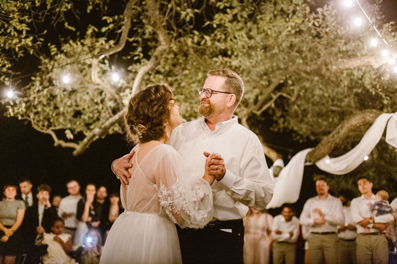 Bride and groom sharing first dance at romantic outdoor evening wedding reception.