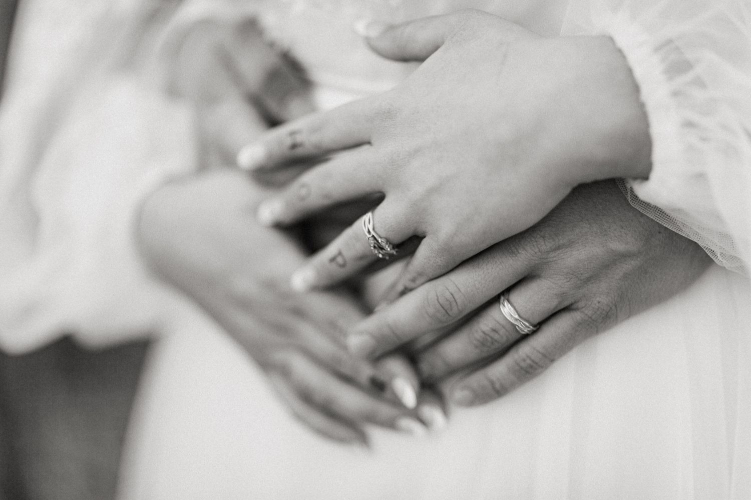 Black and white close-up of bride and groom hands layered together showing wedding rings.