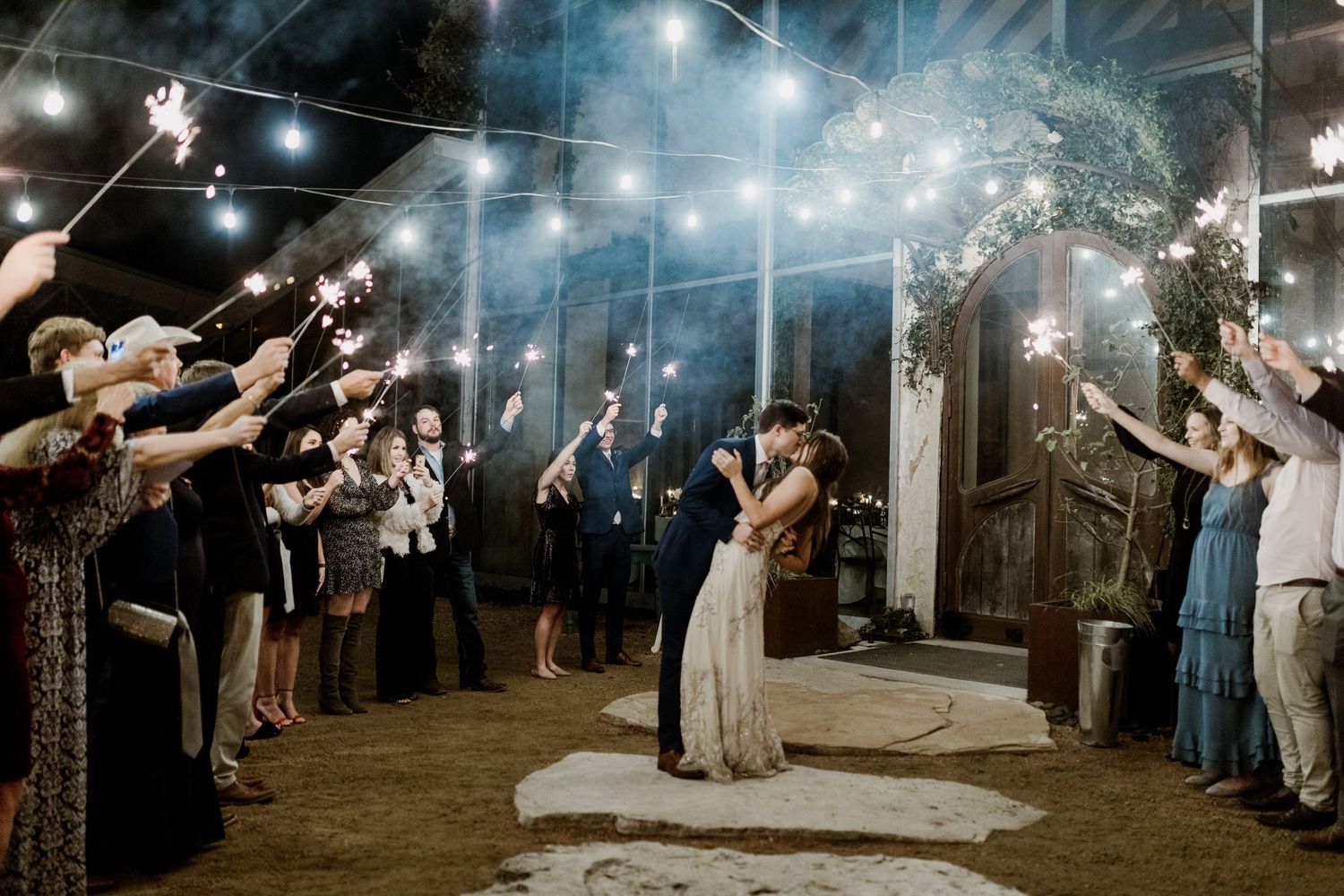 Bride and groom kissing during magical sparkler exit send-off with guests lining the aisle at barn wedding.
