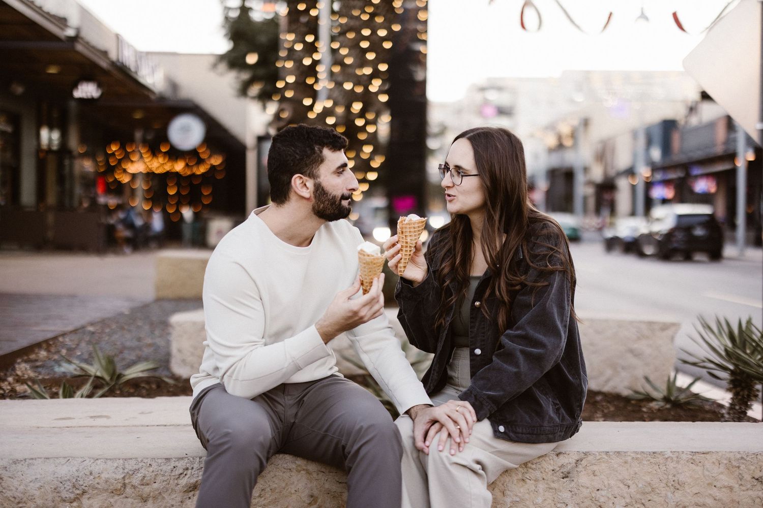 Happy couple sharing ice cream on a city street with festive lights.