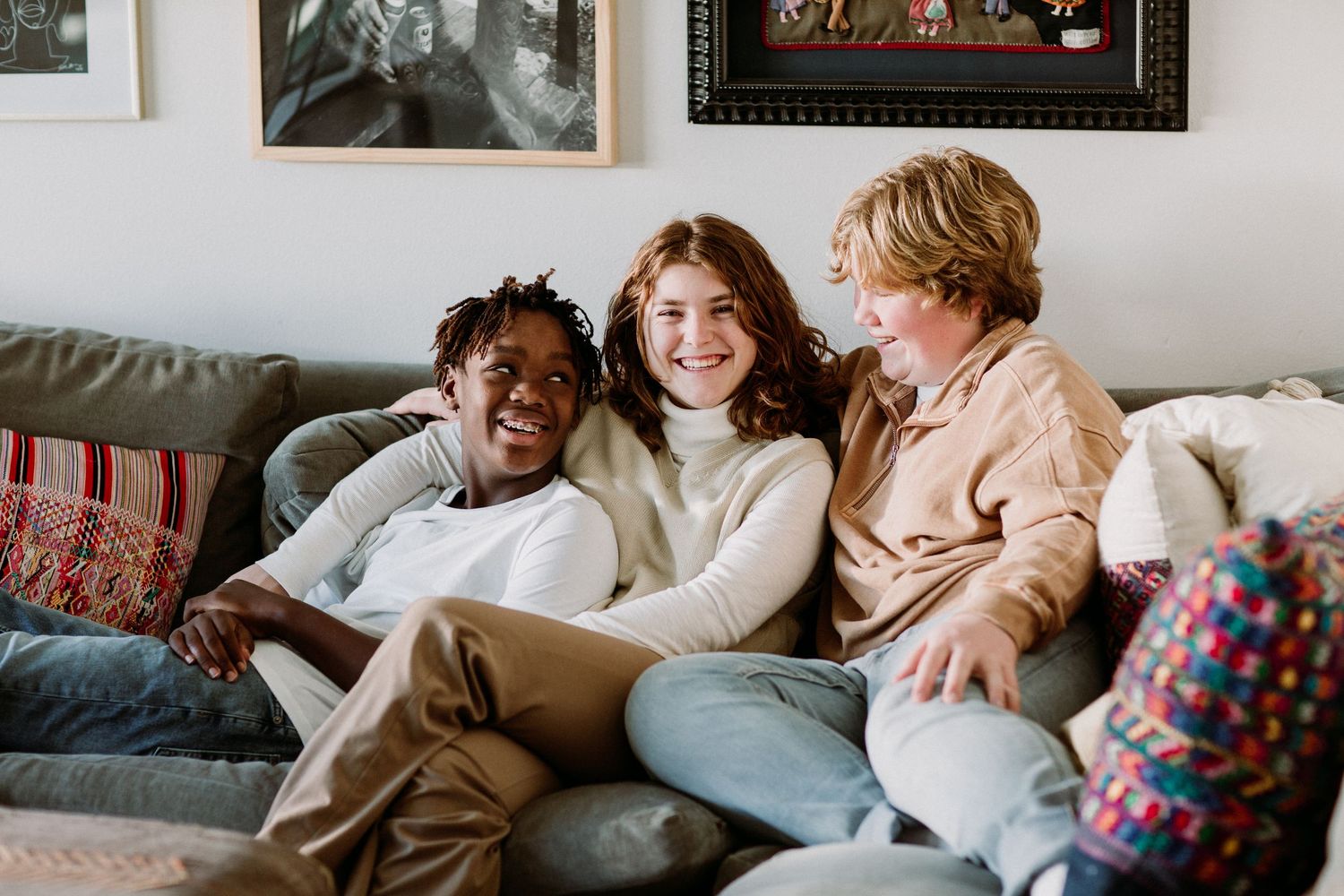 Three diverse teenagers laughing and relaxing together on a cozy sofa.