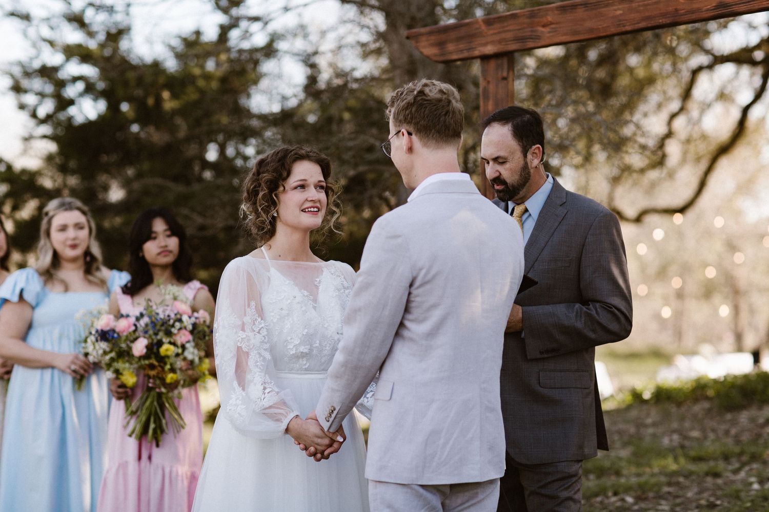 Bride holding colorful bouquet exchanges vows with groom at an outdoor wedding ceremony.