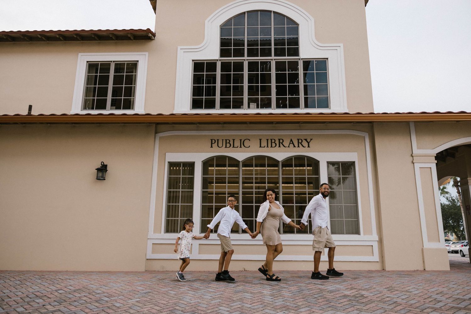 Family of four holds hands while walking in front of a public library building.