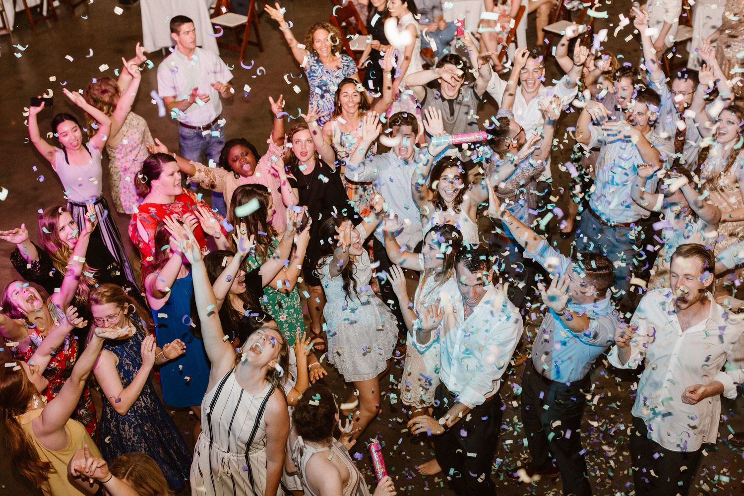 Excited wedding guests dance and cheer with arms raised as confetti fills the air.