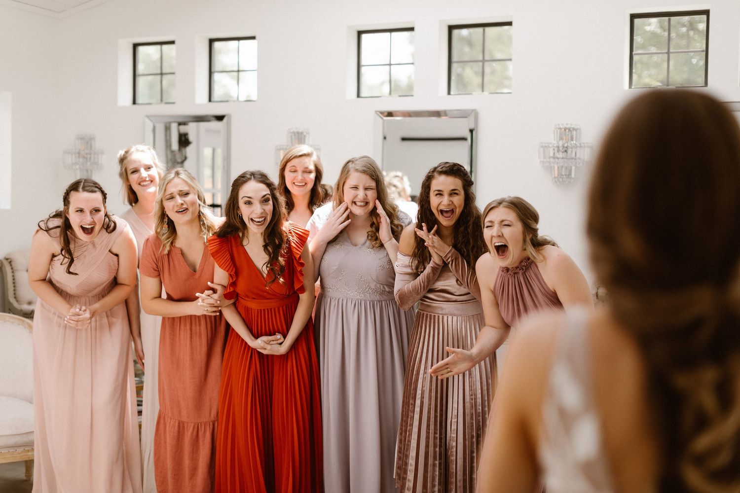 Excited bridesmaids in mismatched pink and red gowns reacting to bride reveal.