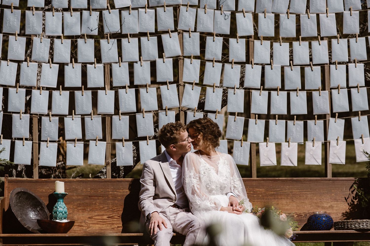 Bride and groom sharing a tender kiss seated before a decorative wall of hanging paper cards at wedding.