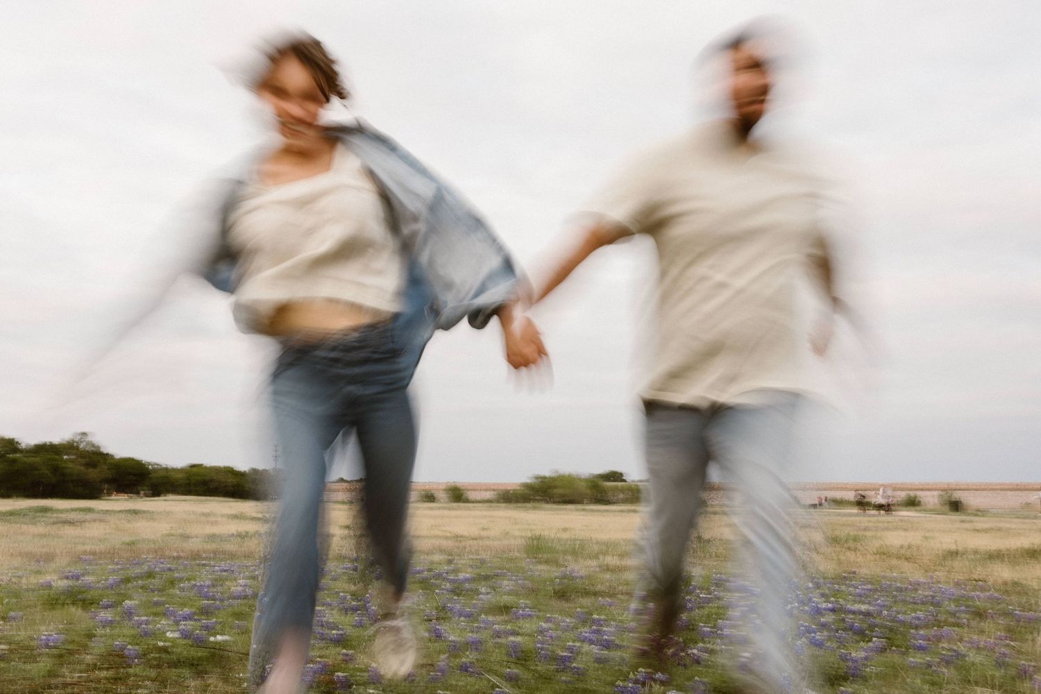 Blurred motion shot of a couple holding hands and running through a wildflower field on an overcast day.
