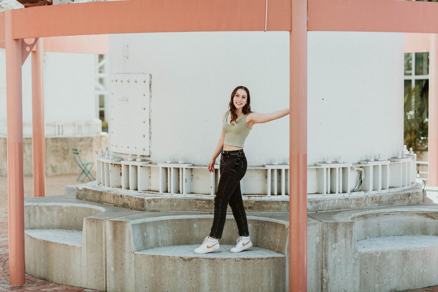 Young woman in crop top and black jeans poses confidently at an outdoor urban architectural structure.