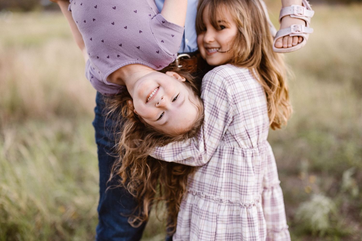 Two young girls with long hair laugh and play together in an outdoor field.