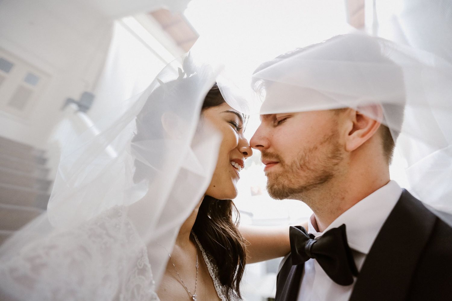Bride and groom sharing intimate moment under flowing veil on wedding day.