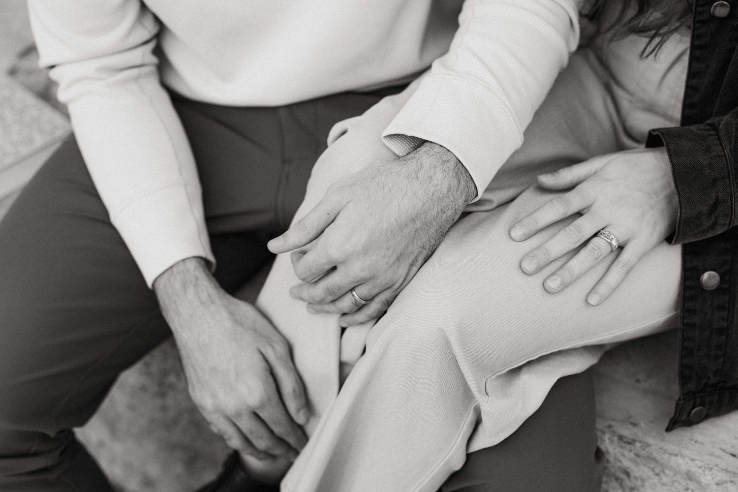 Black and white close-up of a couple holding hands intimately while seated together.