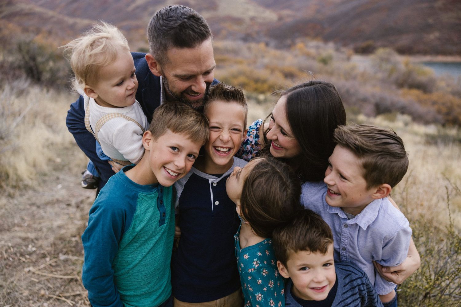A happy family with five children shares a joyful group hug in an outdoor mountain setting.