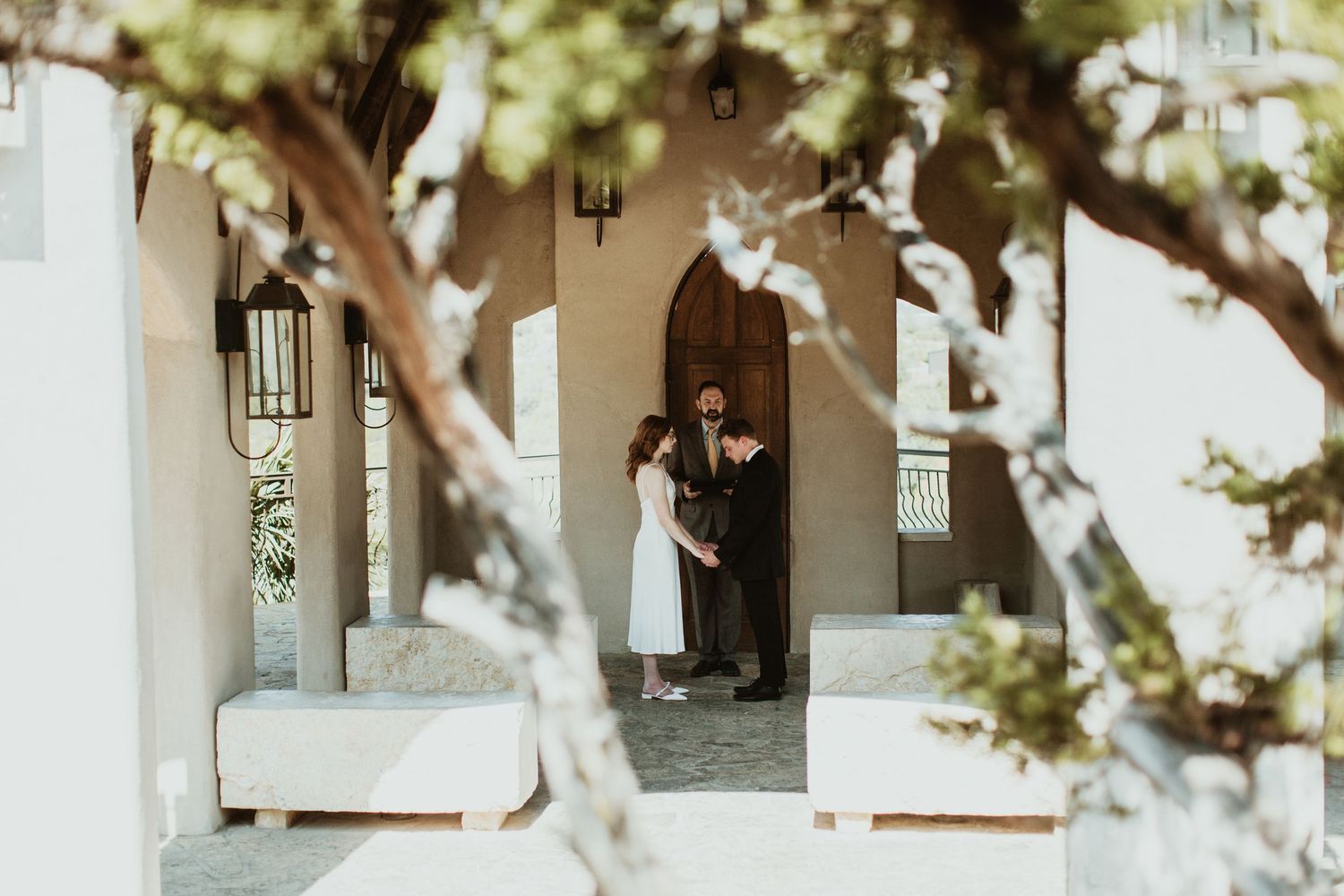 Couple sharing a romantic moment in a doorway of a white Mediterranean-style building framed by trees.