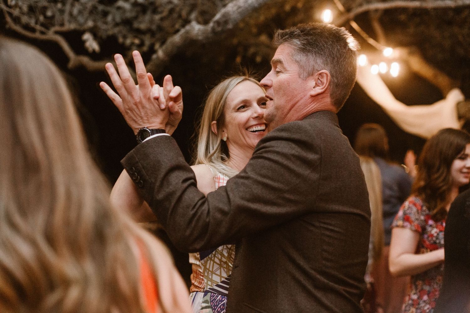 Couple dancing and embracing joyfully at an outdoor wedding reception at night.