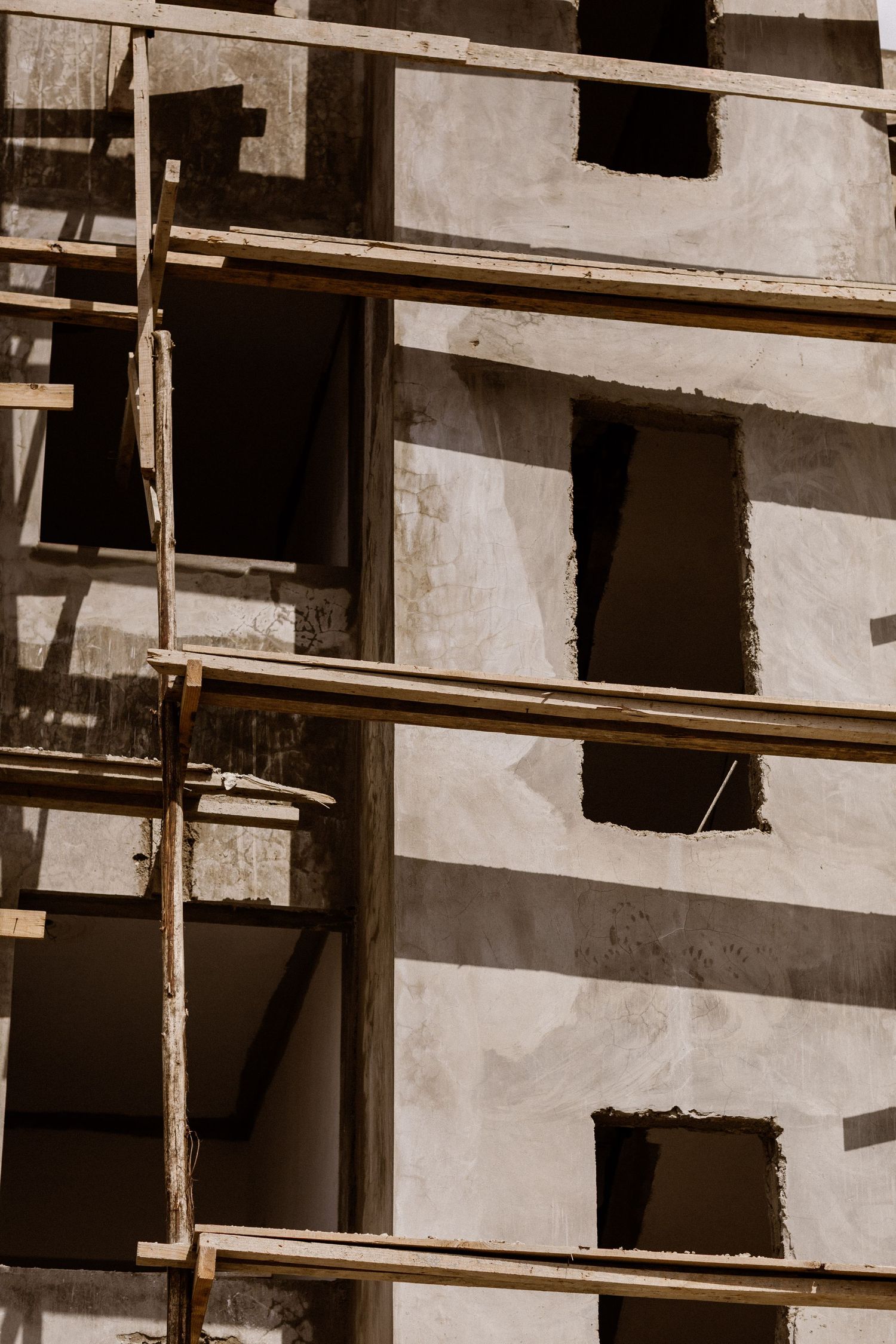 Concrete building under construction with wooden scaffolding and open window frames in sunlight.