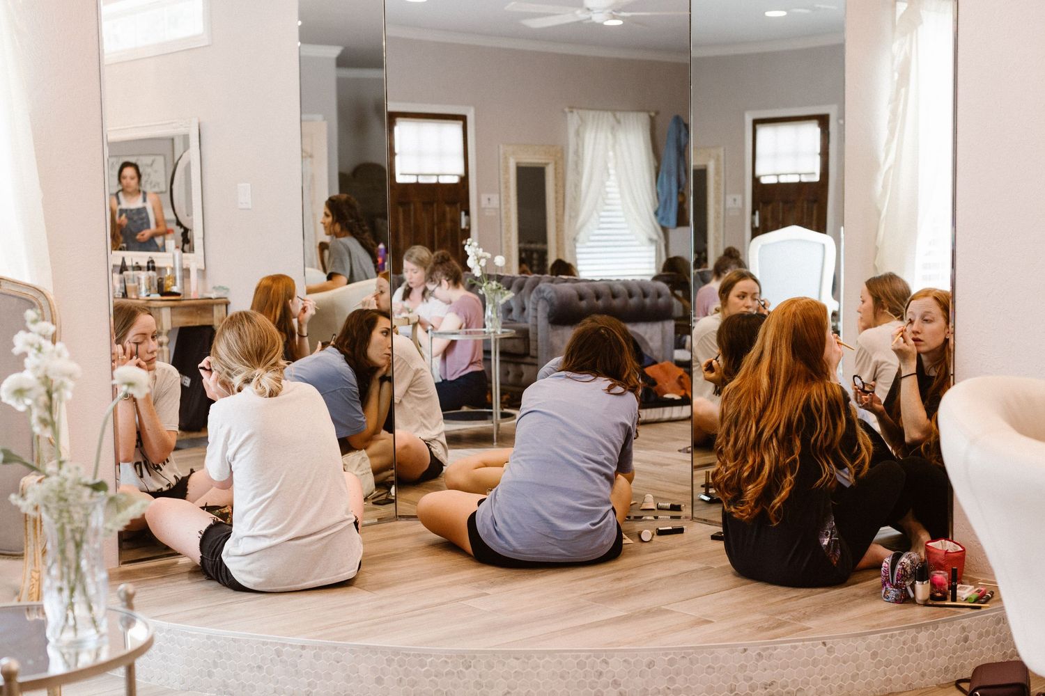 Bridesmaids sitting together on floor in bright salon during wedding morning prep.