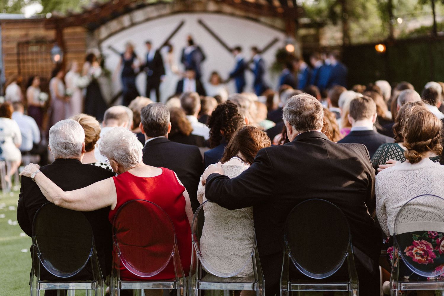 Guests seated outdoors watching a wedding ceremony with the wedding party visible at the altar.