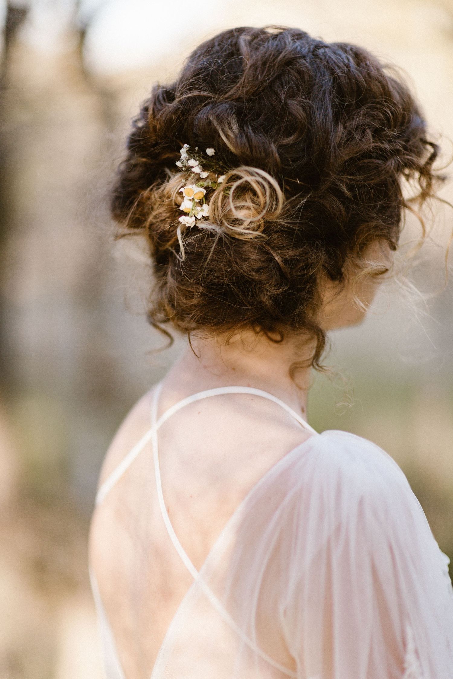 Close-up of bride's curly updo hairstyle adorned with delicate small flowers and hair accessories.