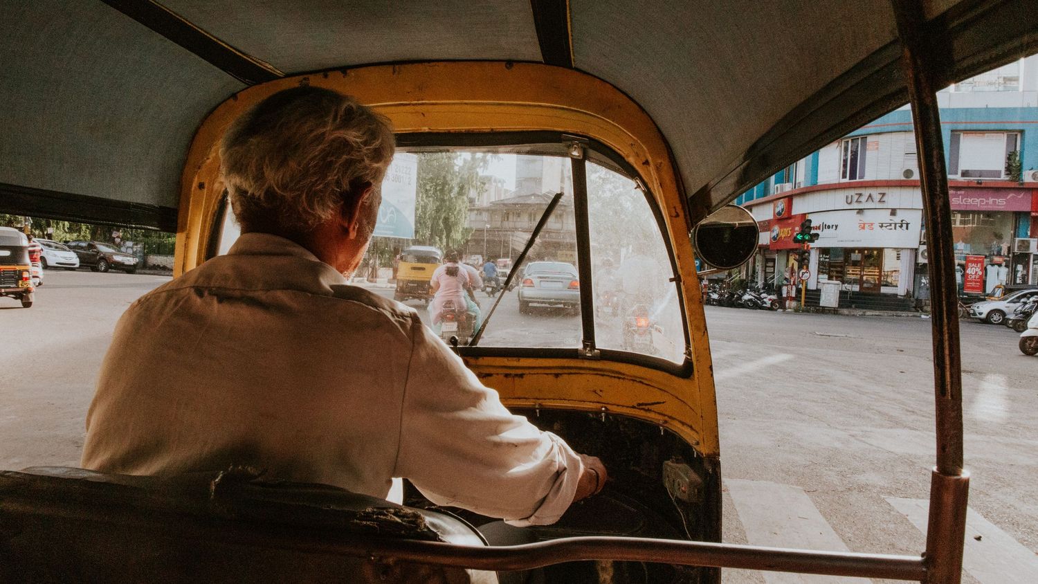 A tuk-tuk driver navigating through busy city traffic viewed from inside the vehicle.